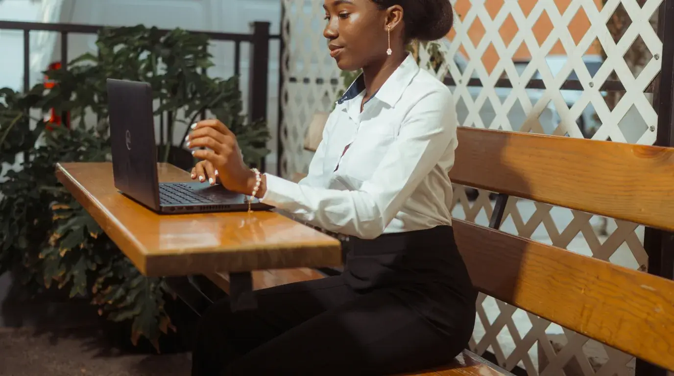 A woman working at a laptop at a wooden table on a planted terrace